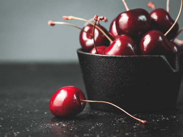 Fresh ruby cherries on black background. Dark moody close up still life - Fotografie, Obrázek