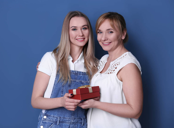 Young woman giving gift box to her mother on color background - Φωτογραφία, εικόνα