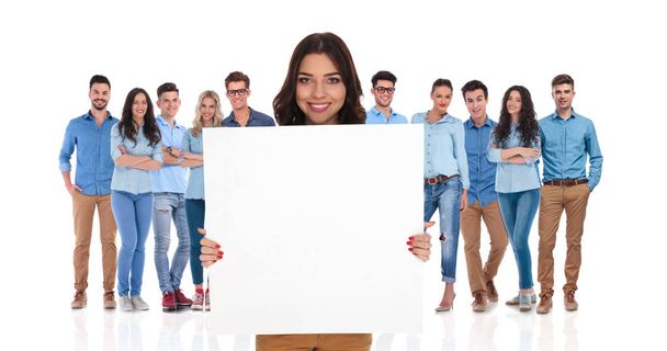 Улыбающаяся бизнес-леди лидер команды держит пустую доску перед своей повседневной группой, стоя на белом фоне
 - Фото, изображение