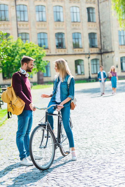 students with backpacks and bicycle standing on street with university on background - Photo, Image