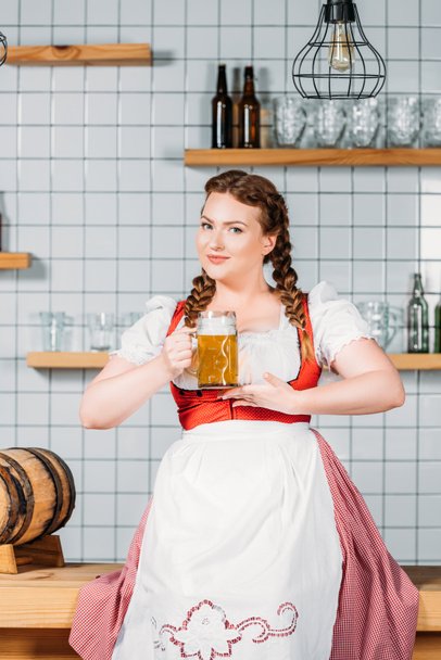 oktoberfest waitress in traditional bavarian dress showing mug of light beer near bar counter - Fotoğraf, Görsel