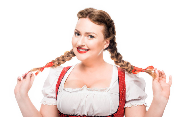aantrekkelijke oktoberfest serveerster in traditionele Duitse jurk tonen pigtails geïsoleerd op witte achtergrond - Foto, afbeelding