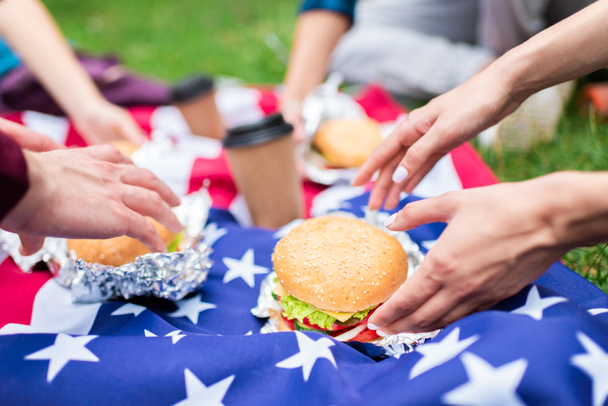 partial view of friends with burgers and american flag on green grass in park - Φωτογραφία, εικόνα