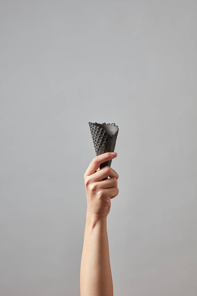 female hand holding an empty black crispy waffle cone on gray background - Foto, Bild