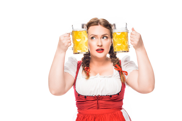 白い背景で隔離のライトビールのマグカップの間に頭を入れて伝統的なバイエルンのドレスでオクトーバーフェスト ウェイトレス - 写真・画像
