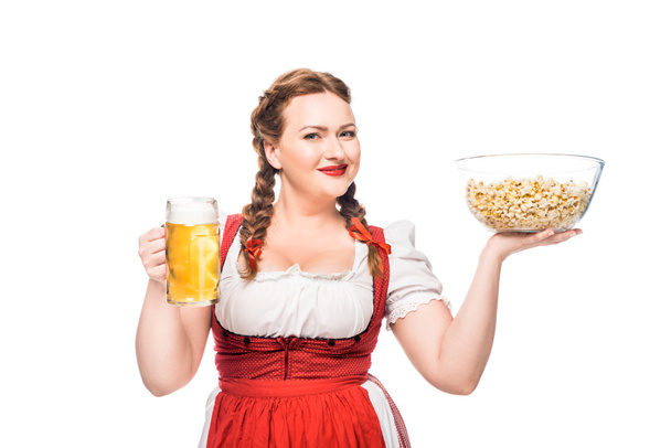 happy oktoberfest waitress in traditional bavarian dress holding bowl of popcorn and mug of light beer isolated on white background - Photo, Image