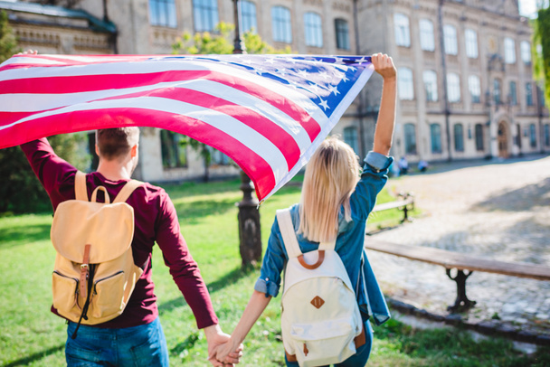 vista trasera de pareja con bandera americana cogida de la mano en el parque
 - Foto, imagen