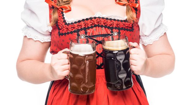 cropped image of oktoberfest waitress in traditional bavarian dress holding mugs with light and dark beer isolated on white background - Foto, Bild