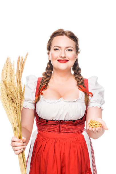 oktoberfest waitress in traditional bavarian dress showing little pretzels and holding wheat ears isolated on white background - Photo, Image