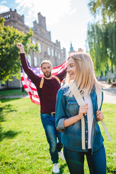 enfoque selectivo de sonriente mujer y novio con bandera americana en las manos en el parque
 - Foto, imagen