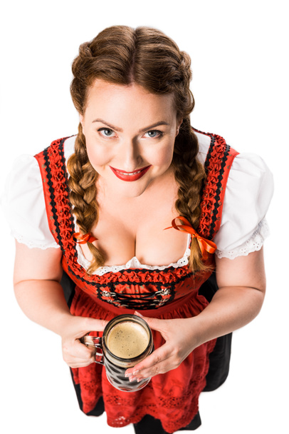 high angle view of smiling oktoberfest waitress in traditional bavarian dress holding mug of dark beer isolated on white background - Foto, afbeelding