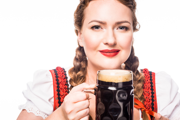 smiing oktoberfest serveerster in traditionele Beierse kleding bedrijf mok van donker bier geïsoleerd op witte achtergrond - Foto, afbeelding