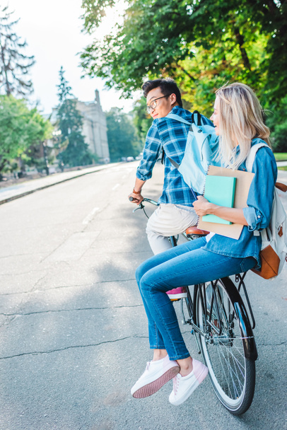 smiling multiracial students riding bicycle together on street - Photo, Image