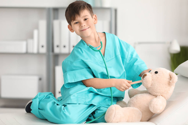 Cute little boy in doctor uniform playing with toy bear in hospital - Fotoğraf, Görsel
