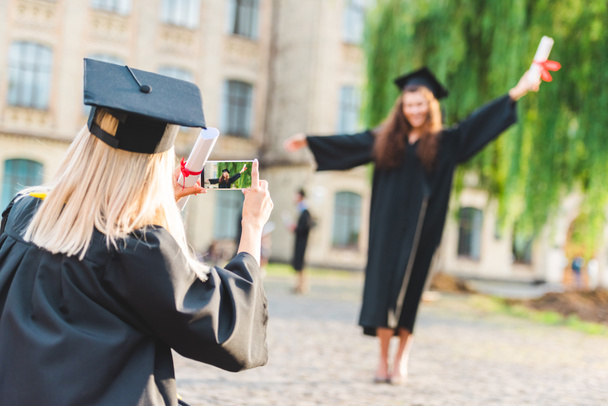 partial view of woman taking picture of classmate with diploma during graduation near university - Photo, Image