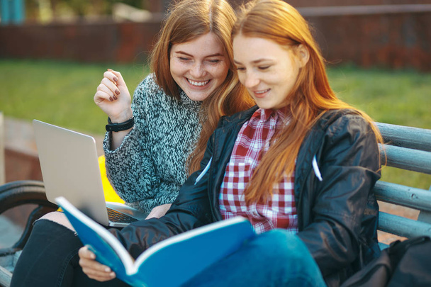Two students sit on bench with laptop and book smiling - Photo, Image