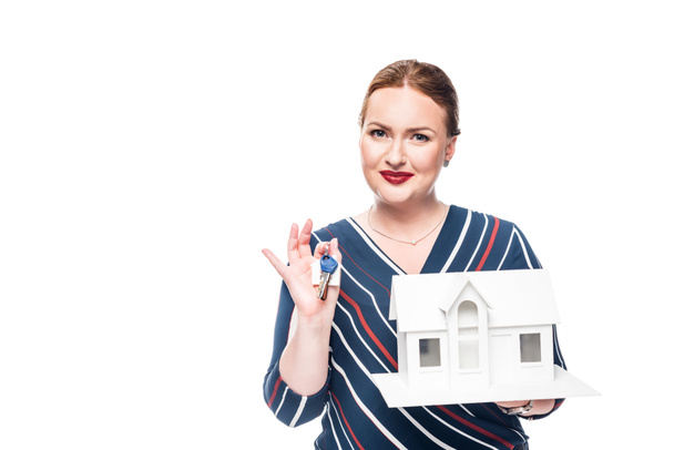 улыбающаяся женщина-агент по недвижимости держит макет дома с ключом изолированы на белом фоне
 - Фото, изображение