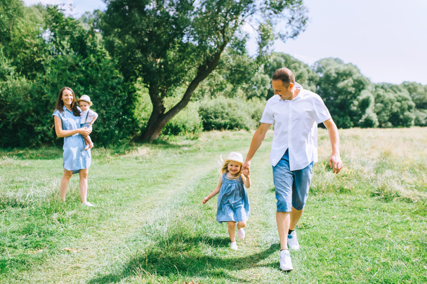father holding hands with daughter and walking with mom and son on summer feild - Foto, immagini