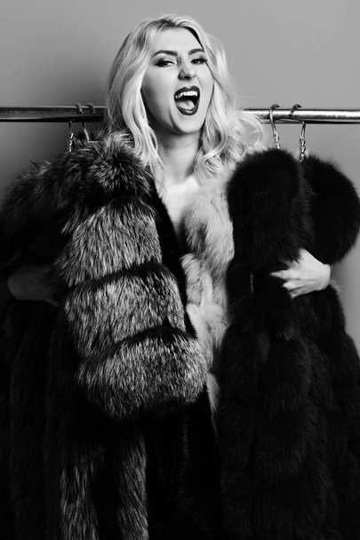 hair standing under rack with golden hangers with fur coats on red studio background. fashionable sexy woman in fur - 写真・画像