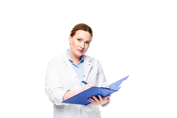serious female doctor in white coat writing in clipboard isolated on white background - Фото, изображение