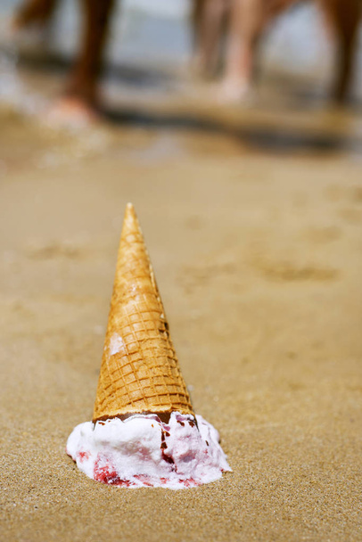 close-up de um cone de sorvete de cabeça para baixo caiu na areia de uma praia
 - Foto, Imagem