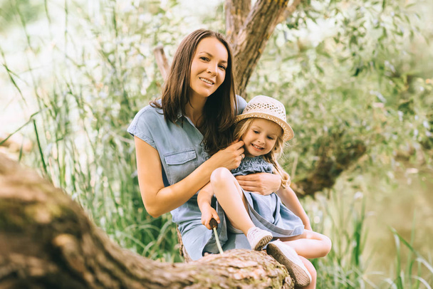 glücklich entzückende Mutter und lächelnde Tochter auf grünem Baum sitzend - Foto, Bild