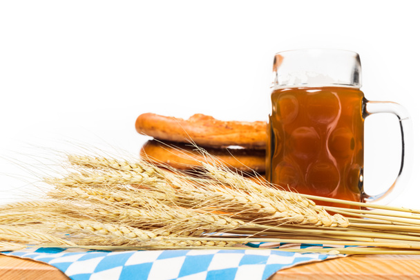 zblízka pohled na uši pšenice, džbánek piva a preclíky na stole s ubrus na bílém pozadí  - Fotografie, Obrázek