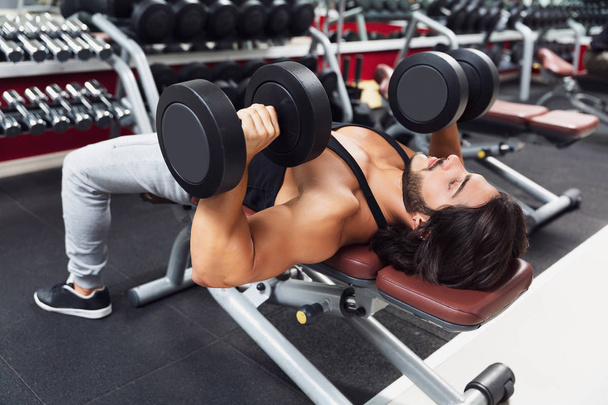 Bodybuilder lying on a bench lifting dumbbell weights in a gym in a concept of health and fitness in a close up upper body view - Photo, Image