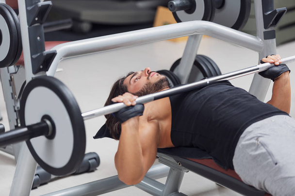 Vzpěrač nebo kulturista ležící na lavičce zvedání činka hmotnosti v tělocvičně při tréninku ve zdravé aktivní životní styl a fitness koncept - Fotografie, Obrázek
