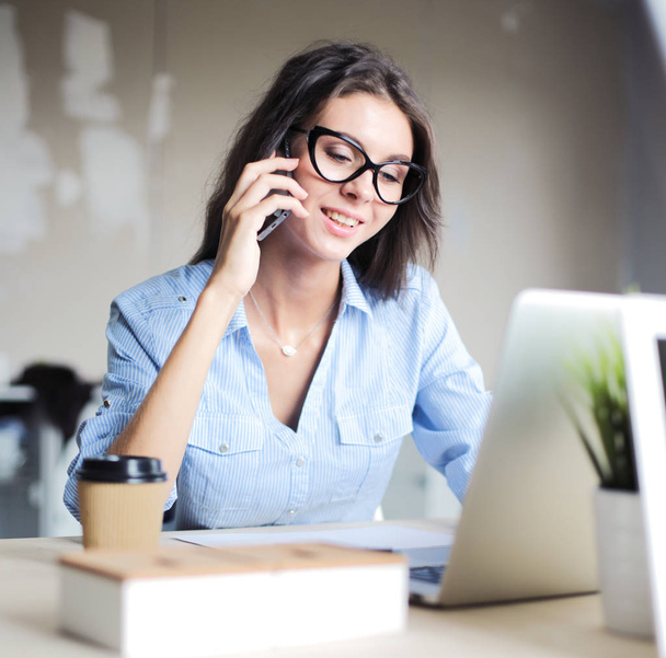 Beautiful young business woman sitting at office desk and talking on cell phone. Business woman - Fotoğraf, Görsel
