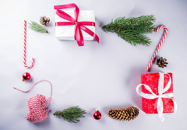 Karácsonyi dekoráció összetétele. Karácsonyi ajándék dobozok, fenyő fa ágai, piros golyó, candy vesszők, a világos szürke háttér. Lapos feküdt, top view. - Fotó, kép