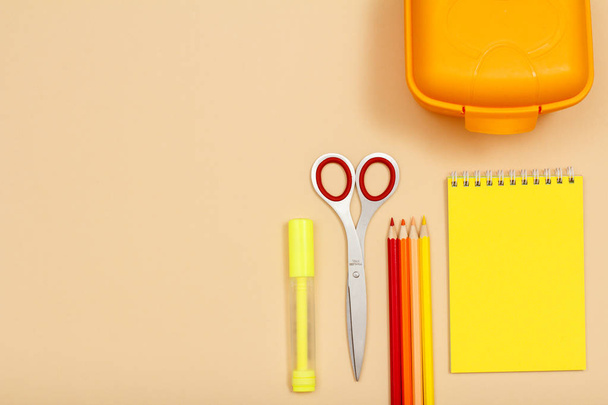 Stylo feutre, ciseaux, crayons de couleur, boîte à lunch et carnet sur fond beige. Vue de dessus. Retour à l'école. Fournitures scolaires
 - Photo, image