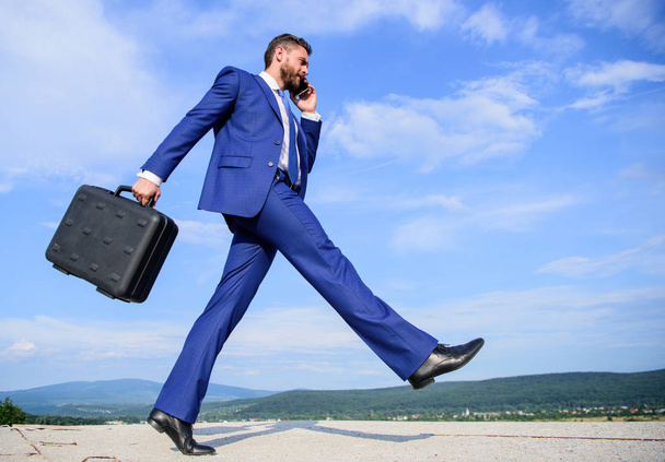 Businessman formal suit carries briefcase sky background. Businessman solving business problems on phone. Never stop. Keep going towards your goal. Entrepreneur in motion purposeful expression - Foto, Imagem