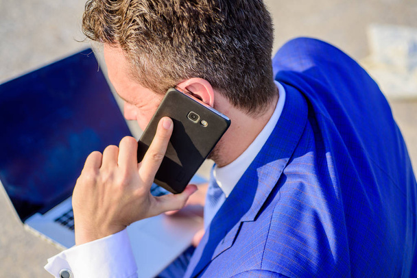 Call technical support service. Businessman holds smartphone near ear close up. Consultation and help concept. How can I help you. Man formal suit call support while works with laptop rear view - Photo, Image