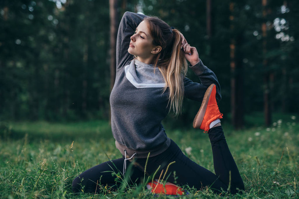 Nuori nainen harjoittelee joogaa tekemällä yksijalkainen kyyhkynen poseeraa nurmikolla puistossa
 - Valokuva, kuva