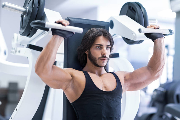 Fit volwassen bodybuilder met shoulder press machine in een sportschool uit te werken tijdens de opleiding in een gezonde actieve levensstijl en fitness concept - Foto, afbeelding