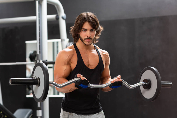 Homem musculoso forte trabalhando com um sino em um ginásio e olhando seriamente para a câmera
 - Foto, Imagem