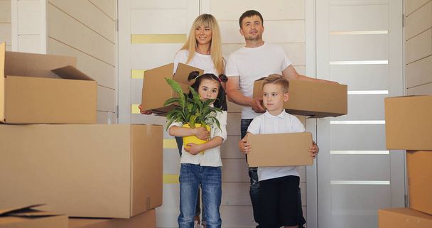 Happy family with two children at new home. Family with cardboard boxes in new house at moving day. Mother father and child in new house . - Foto, imagen
