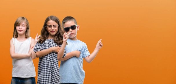 Group of boy and girls kids over orange background very happy pointing with hand and finger to the side - Photo, Image