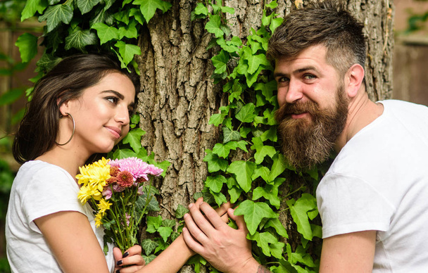 Man bearded hipster holds hand girlfriend. Couple in love romantic date walk nature tree background. United with nature. Couple in love lean on trunk with ivy. Pleasant date in nature environment - Zdjęcie, obraz