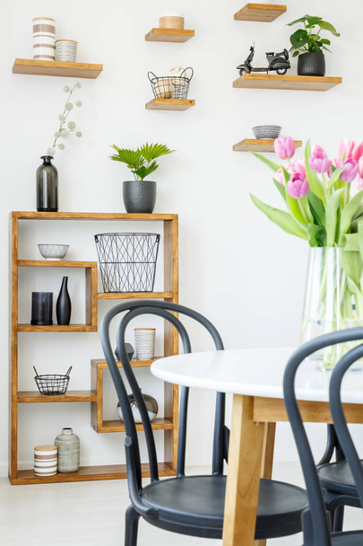 Close-up of a black chair and white table with tulips, and decorated shelves in the background - Foto, imagen