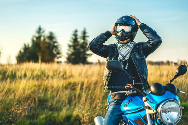 Biker putting helmet on head while sitting on sport motorcycle outdoor on road - Photo, image
