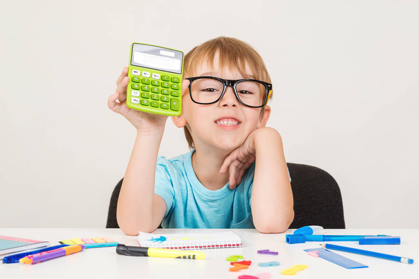 Smart boy using calculator. Kid in glasses figuring out math problem. Developing logical skills. Happy school boy doing homework. Smart kid in glasses at table with school supplies. Back to school - Photo, Image