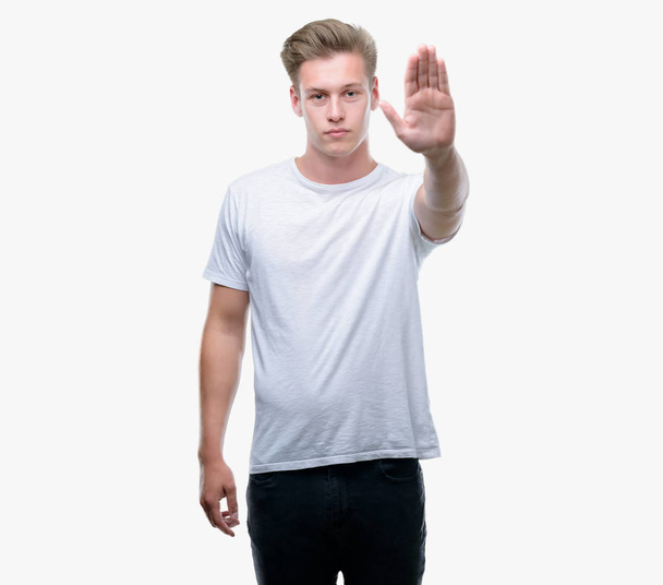 Молодой красивый блондин с открытой рукой делает знак стоп с серьезным и уверенным выражением лица, защитный жест
 - Фото, изображение