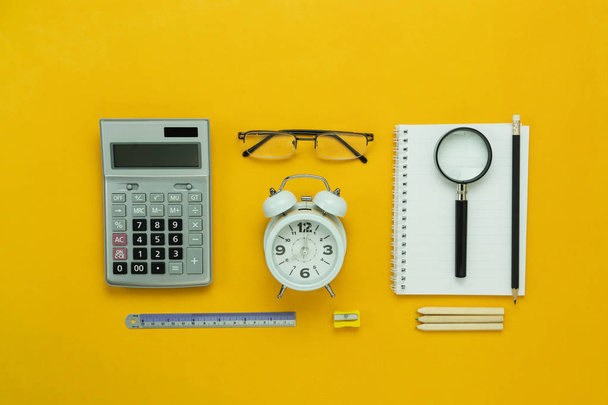 Table top view aerial image of back to school of education season background concept.Flat lay accessories for business finance the clock & calculator and objects on modern rustic yellow paper. - Foto, immagini