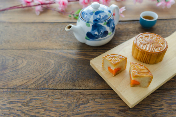 Közelkép arculatának étel desszert dekorációk kínai Hold Fesztivál háttér koncepció. Élelmiszer & ital a torta, tea-cup és rózsaszín virág a modern, rusztikus, fából készült deszka. Szabad hely a design a szöveg hozzáadása. - Fotó, kép