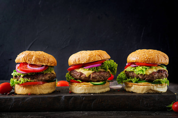 Três hambúrgueres com carne de vaca e legumes frescos no fundo escuro com espaço de cópia
 - Foto, Imagem