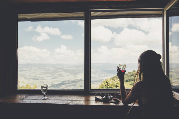 stylová holka cestující sedící u okna s výhledem na hory a nebe. Happy bederní žena držící nápoj, při pohledu na oblohu a relaxaci. Letní dovolená koncept. cestování a toulavost - Fotografie, Obrázek