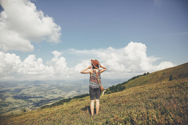 мандрівник хіпстер дівчина в капелюсі, ходить в сонячних горах, дивлячись на хмари на небі. літні канікули. простір для тексту. щасливий атмосферний момент. стильна жінка подорожує
 - Фото, зображення