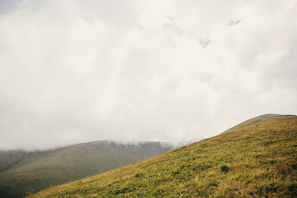 bela colina com grama em nuvens nebulosas e nevoeiro, montanhas ensolaradas. paisagem paisagem de colinas na luz da manhã, com nuvens. viagens de verão
 - Foto, Imagem